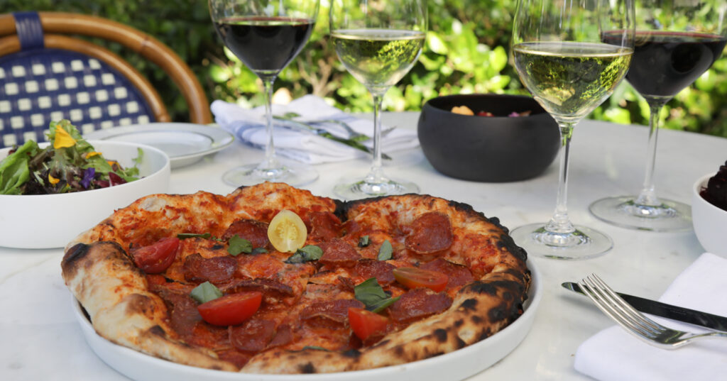 pizza, green salad and wine glasses on white outdoor table