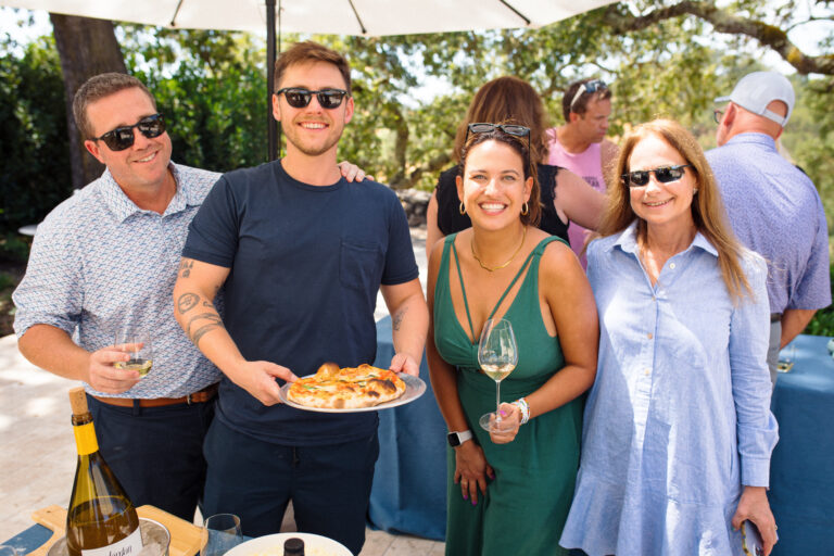 group of men and women smiling with wood fired pizza and glass of wine