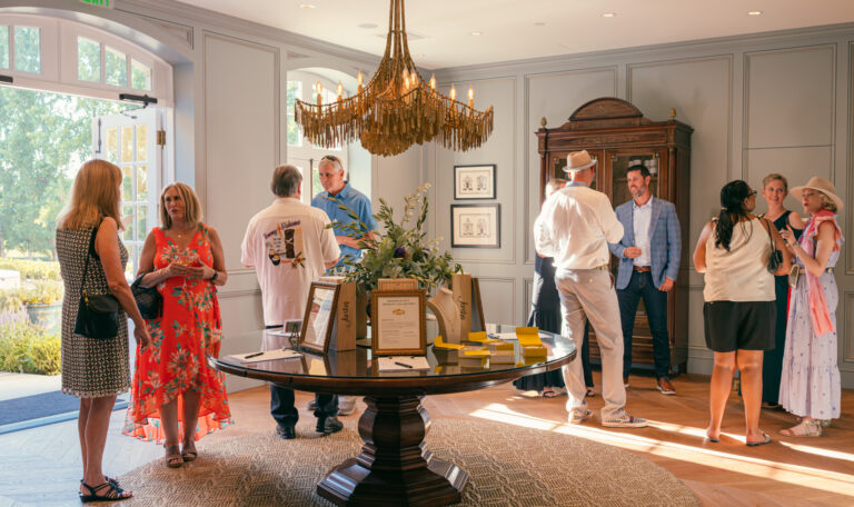 A group attending the starlight supper standing in Jordan lobby salon around antique French table with a gold chandelier overhead.