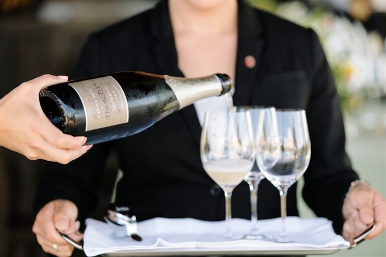 bottle of champagne pouring into wine glasses on service tray