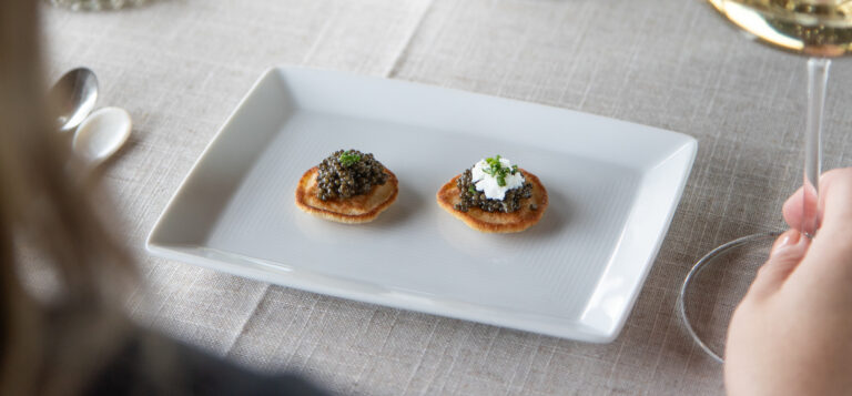 caviar on blinis on white plate with glass of champagne