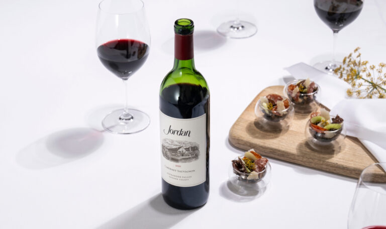 bottle of jordan cabernet sauvignon on white table with glass dishes of hors d'oeuvre arranged around the bottle and a wooden serving platter