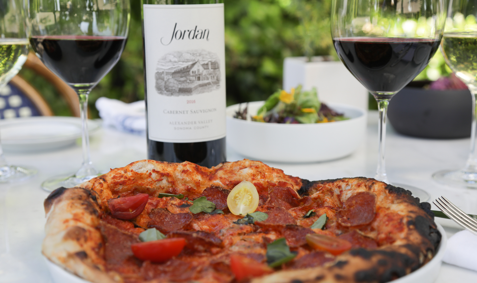 freshly made pizza on plate on table with bottle of jordan cabernet sauvignon