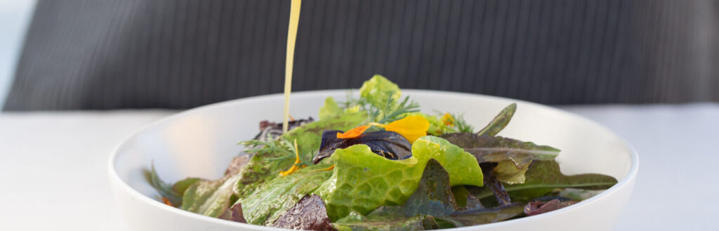 chef hand pouring vinaigrette onto a green salad