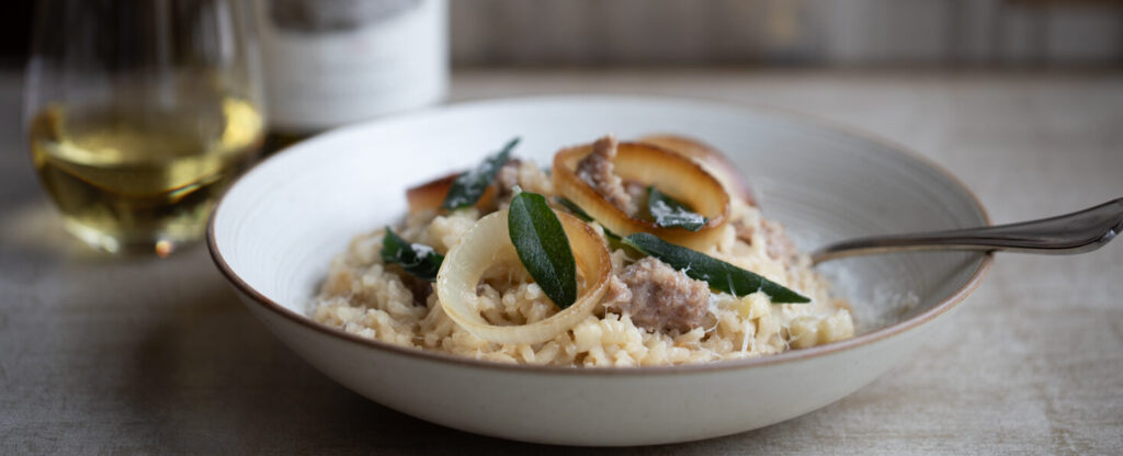 risotto with sage leaves and onion in a bowl with a glass and bottle of chardonnay