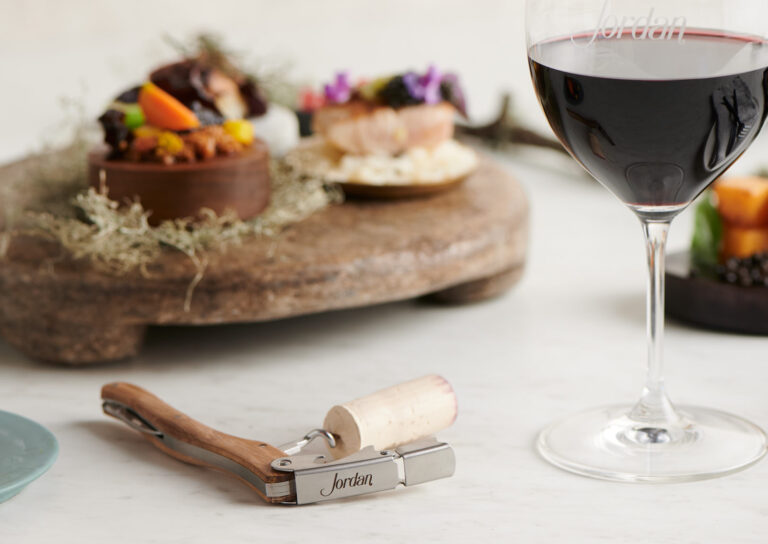 corkscrew with cork and wine glass on white table